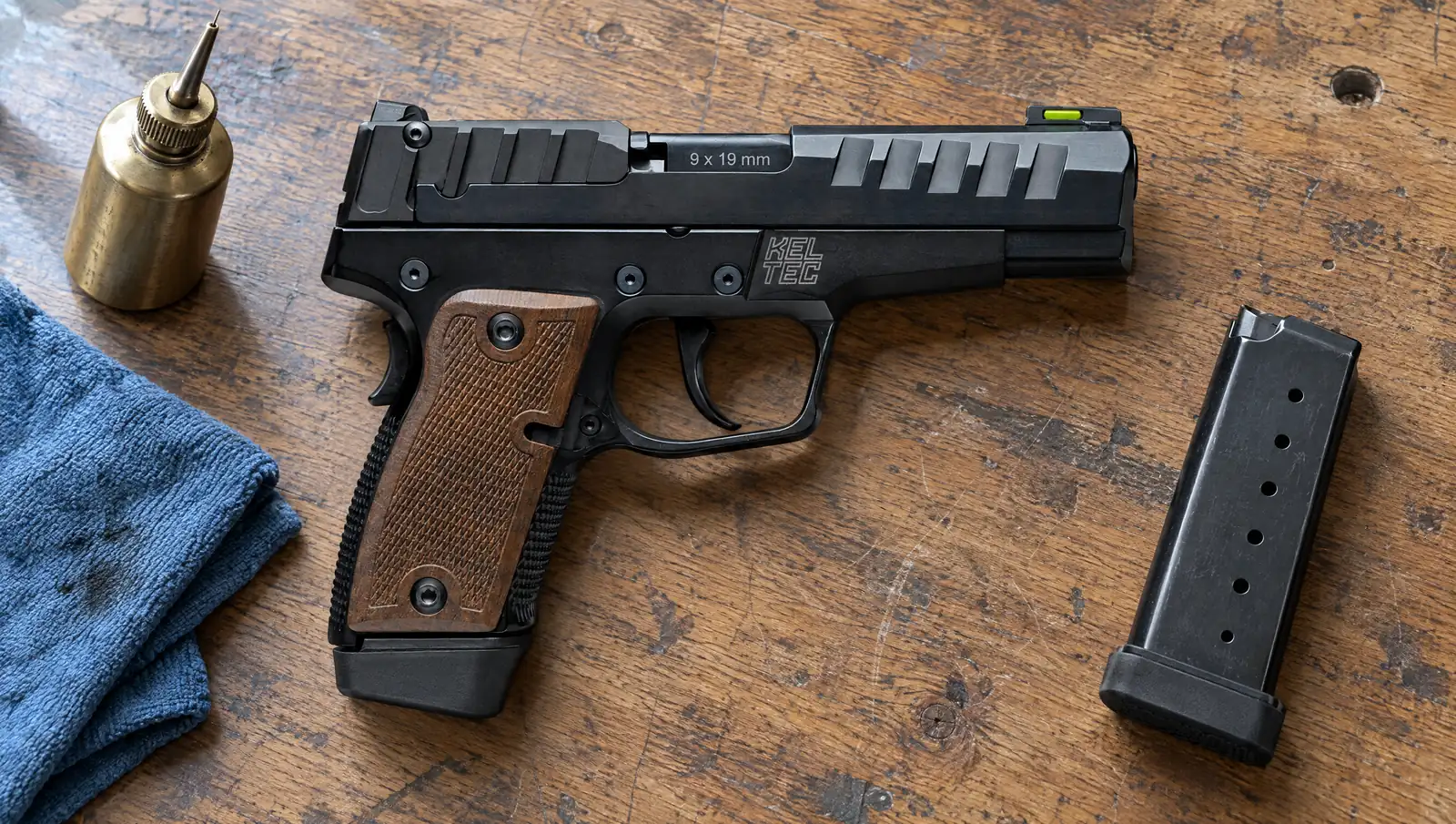 Kel-Tec P15 Metal 9mm pistol with a black metal frame and checkered walnut grip panels lying on an oak workbench beside a brass oiler, a shop rag and a spare magazine