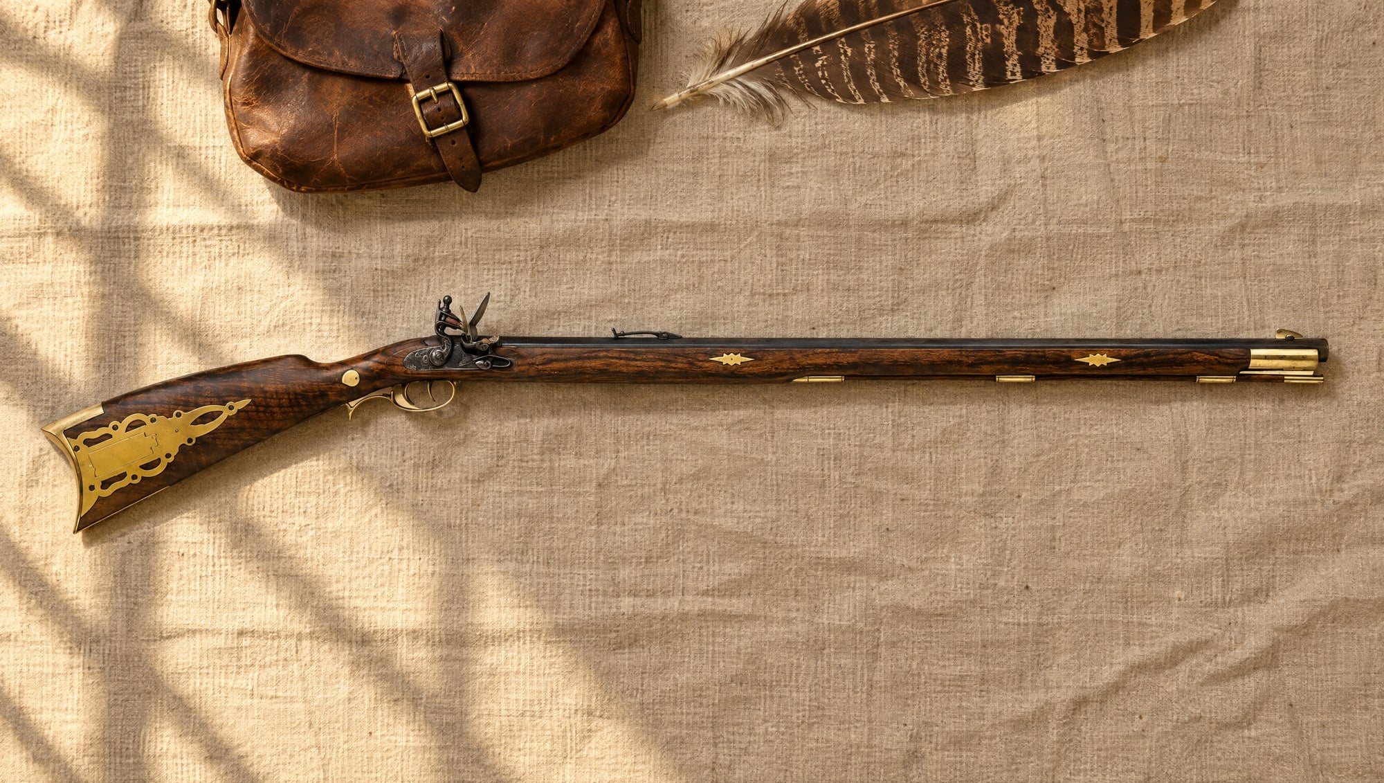 Kentucky rifle: a Traditions Pennsylvania flintlock long rifle lying flat on linen beside a leather hunting bag and a turkey feather