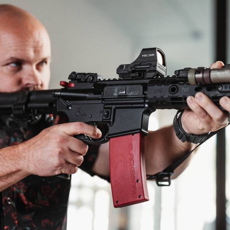 Shooter aiming an AR-15 fitted with a Mantis BlackbeardX and red magazine