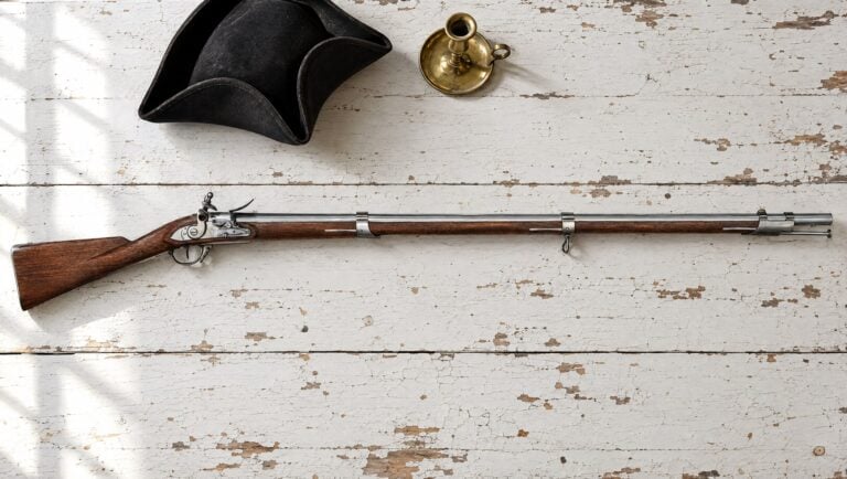 Muskets: a Pedersoli 1795 Springfield flintlock musket lying flat on a white painted table beside a tricorn hat and a brass candlestick