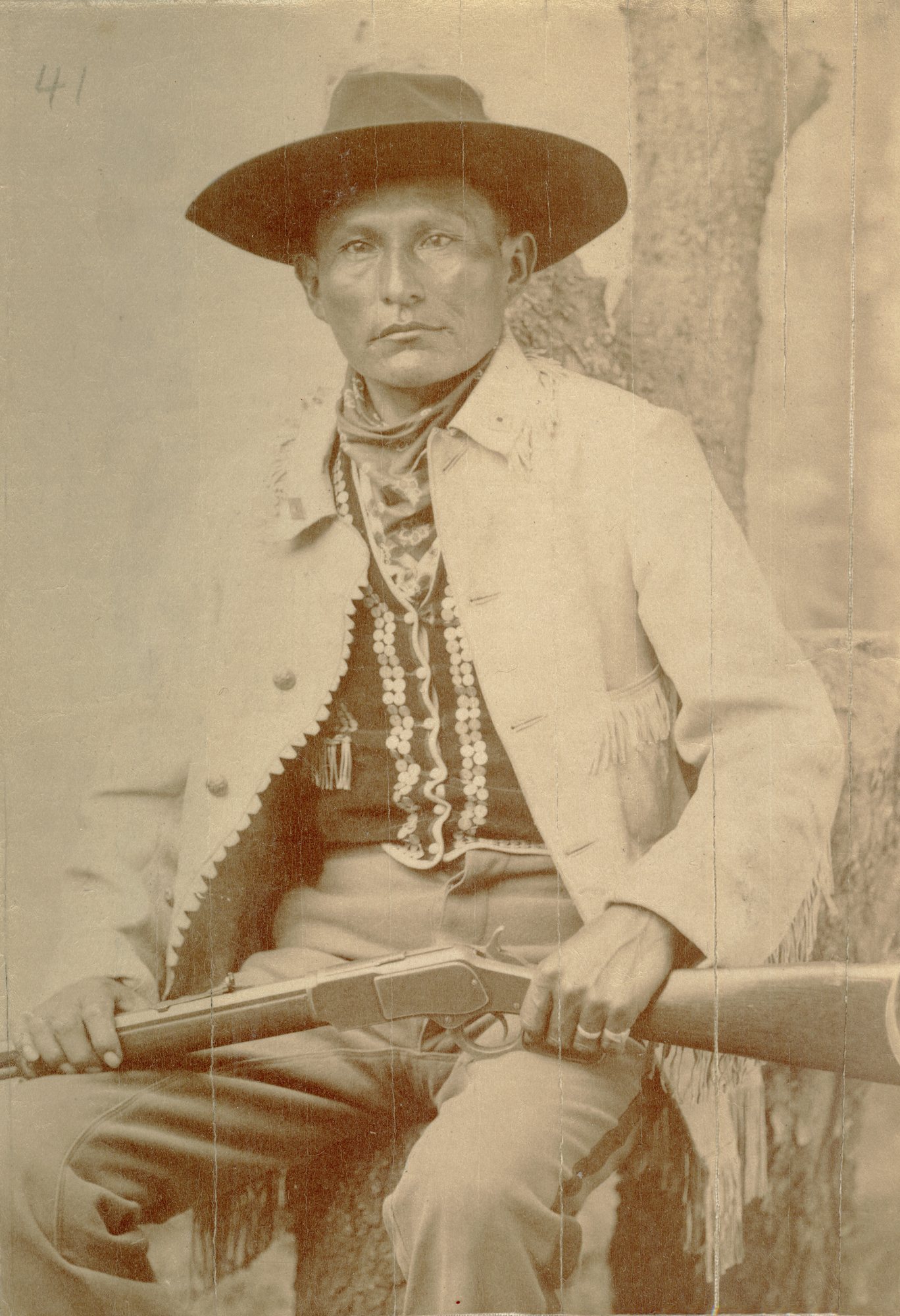 Portrait from the 1890s of Naiche seated with a lever-action rifle across his knees