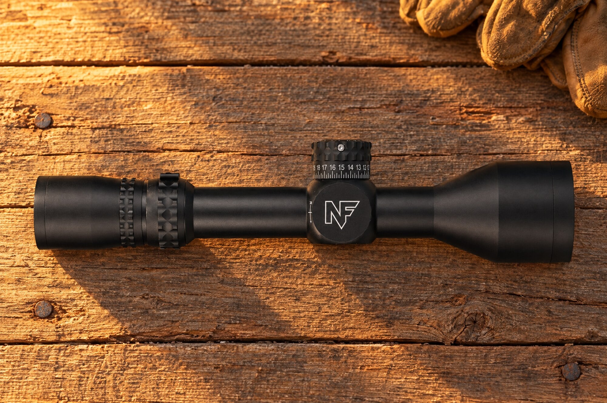 Nightforce NX8 2.5-20 power first focal plane rifle scope lying on a cedar plank shooting bench at golden hour