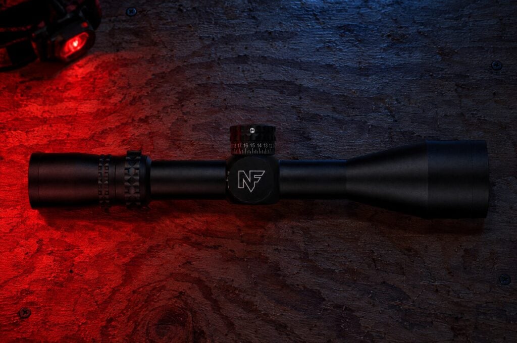 Black Nightforce NX8 4-32 power second focal plane rifle scope on a plywood shooting barricade under red headlamp light