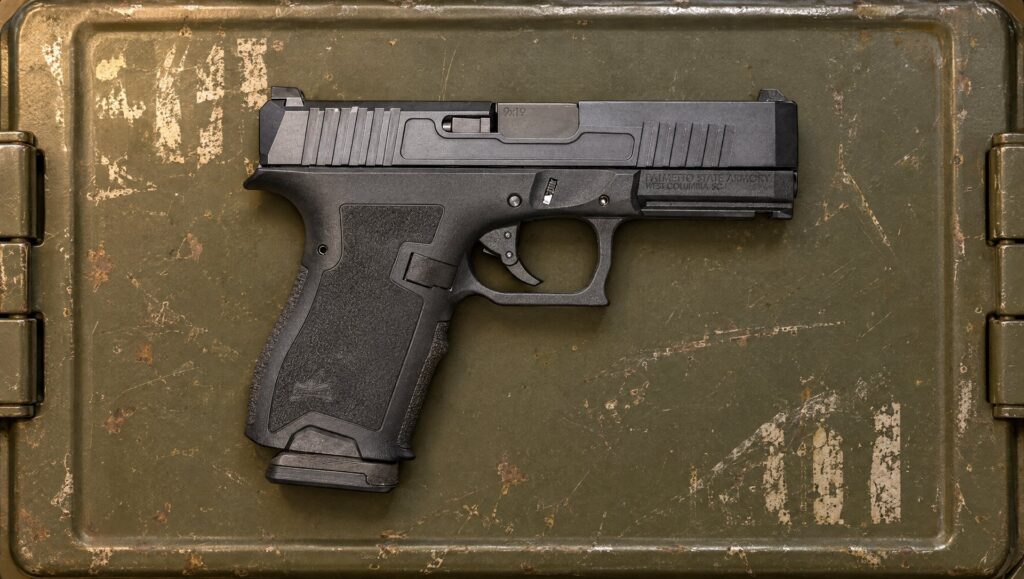 Black PSA Dagger Compact pistol lying on a steel ammo can lid in a garage workshop
