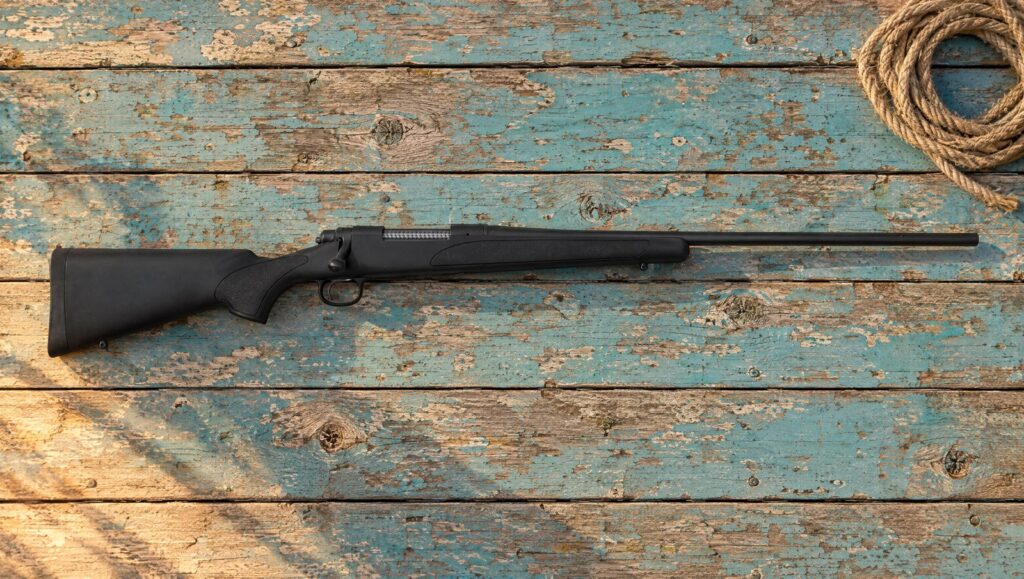 Remington 700 ADL with plain black synthetic stock, blind magazine and matte blued barrel lying flat on weathered blue painted planks