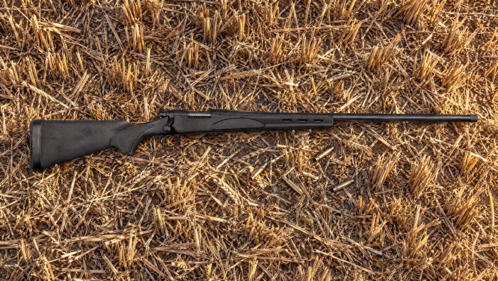 Remington 700 ADL Varmint with heavy threaded barrel and black synthetic stock with vented beavertail forend lying flat on wheat stubble
