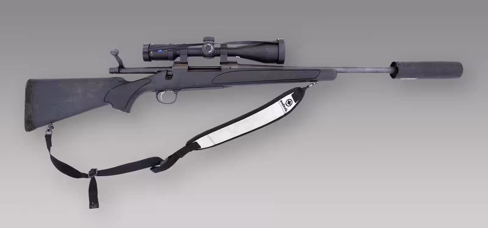 Remington Model 700 bolt-action rifle with a synthetic stock, scope, sling and suppressor on a gray background