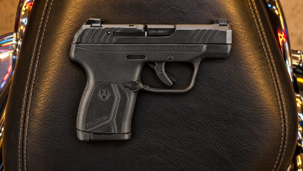 Black Ruger LCP Max pistol lying on a leather motorcycle seat at a gas station at night