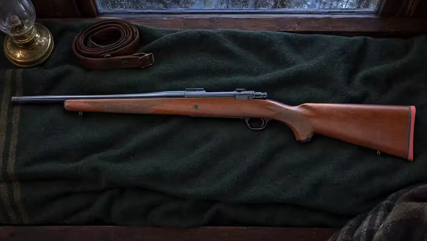 Ruger M77 Hawkeye Hunter with 16.6 inch blued barrel and walnut stock lying on a green wool blanket beside an oil lamp and a leather sling