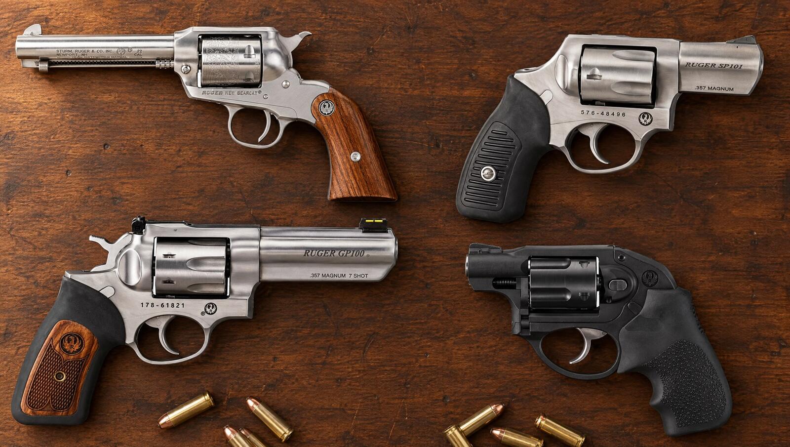 Ruger New Bearcat, SP101, GP100 and LCR revolvers laid flat on a walnut bench with loose cartridges