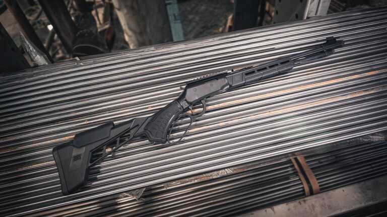 Savage Revel Tactical lever action rimfire rifle with black MDT stock lying on a rack of steel bar stock