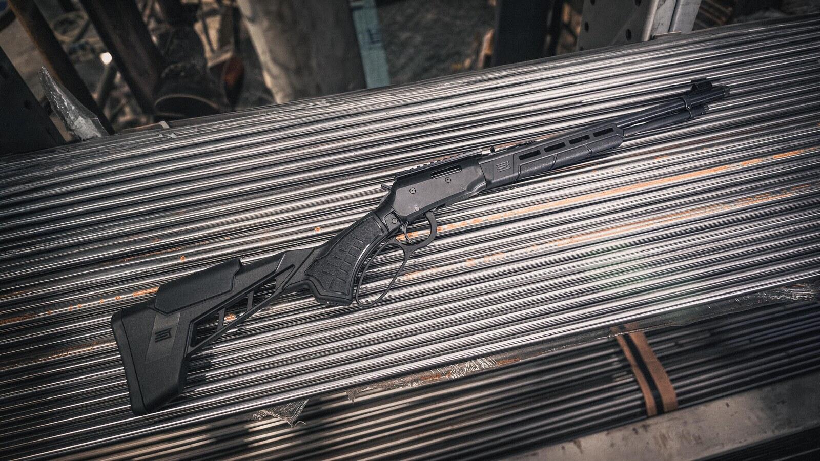 Savage Revel Tactical lever action rimfire rifle with black MDT stock lying on a rack of steel bar stock