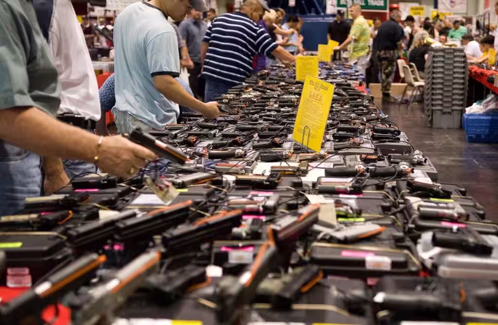 Long table of handguns for sale at a gun show in Houston, with buyers looking them over