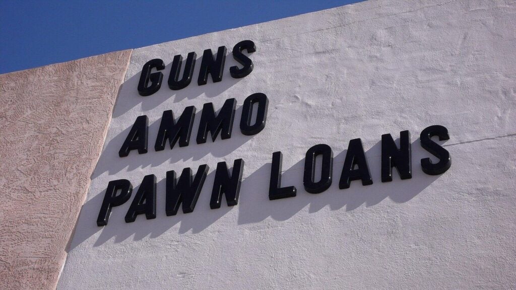 Hand-painted sign reading Guns Ammo Pawn Loans on a white wall