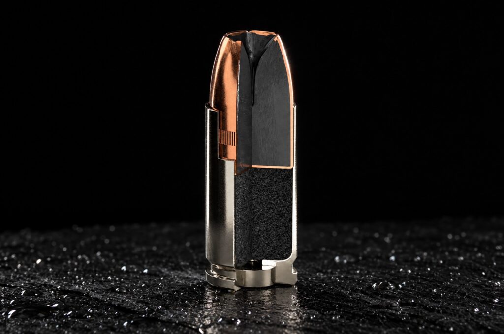 Sig V-Crown 9mm cutaway cartridge showing the V-shaped cavity, narrow lower channel and toothed cannelure on black slate