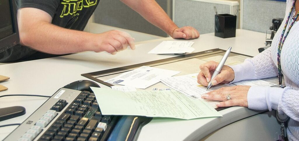 Two people at a counter, one signing a paper form with a pen