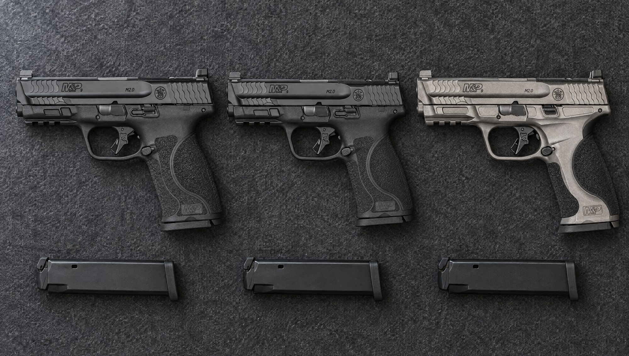 Smith & Wesson M&P M2.0 models compared: black M&P9 M2.0 Full Size, black M&P9 M2.0 Compact and gray M&P9 M2.0 Metal lying flat on a gray felt mat