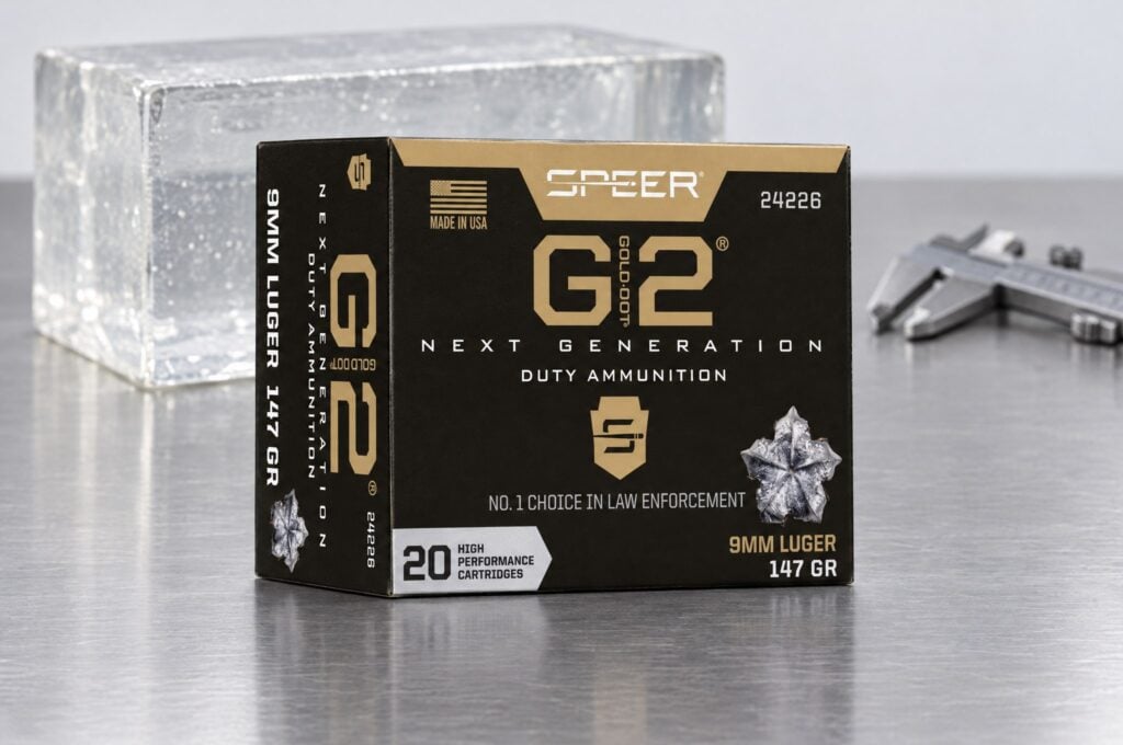 Speer Gold Dot G2 9mm Luger 147 gr box on a steel lab table beside a clear ballistic gelatin block and calipers