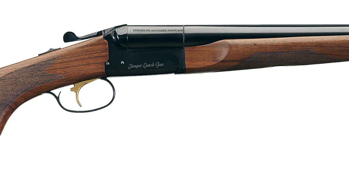 Close-up of a walnut Stoeger Coach Gun receiver showing the Stoeger Coach Gun script, top lever, tang safety and gold single trigger, Stoeger photo