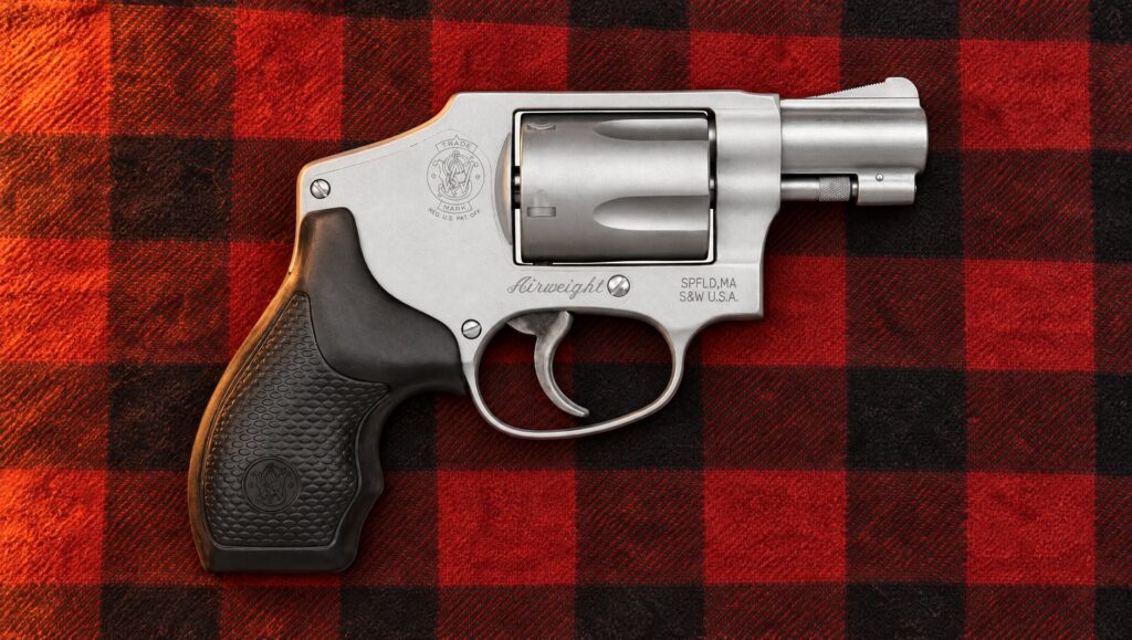 Smith and Wesson 642 Airweight revolver lying on a buffalo plaid flannel shirt by firelight