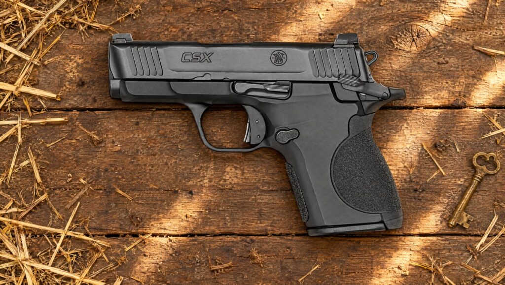 Black Smith and Wesson CSX pistol lying on weathered barn wood with hay and an old brass key