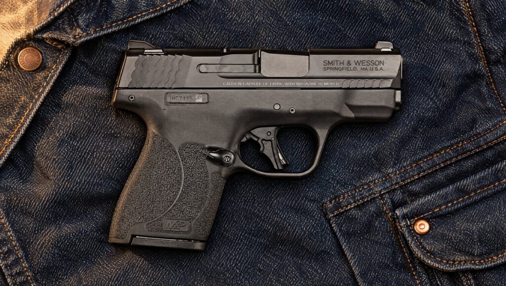 Black Smith and Wesson M&P Shield Plus pistol lying on a folded denim jacket under warm porch light