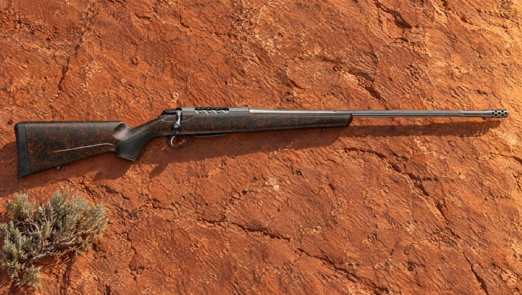 Tikka T3x Lite Roughtech Ember with orange web stock, fluted stainless barrel and muzzle brake lying flat on red sandstone