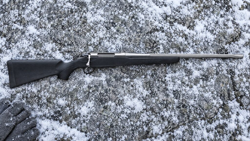 Tikka T3x Superlite with fluted stainless barrel and black synthetic stock lying flat on snow-dusted granite
