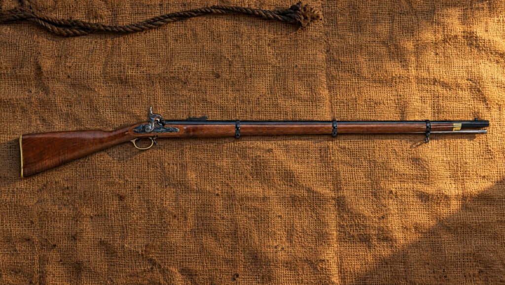 Traditions 1853 Enfield percussion rifle-musket with brass furniture lying flat on brown burlap in evening light