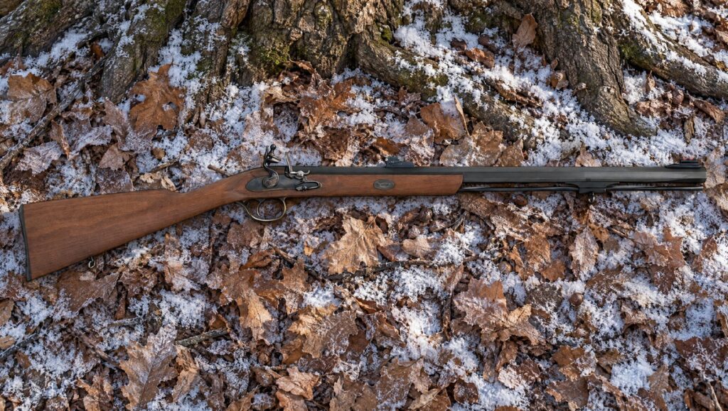 Traditions Deerhunter flintlock rifle with a hardwood stock lying on frosted leaves in deer woods