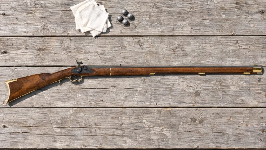 Traditions Kentucky percussion rifle lying flat on a sun-bleached wooden shooting bench with patches and lead balls