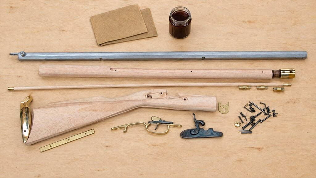 Traditions Kentucky rifle kit parts laid out flat: barrel, unfinished stock pieces, lock and brass furniture