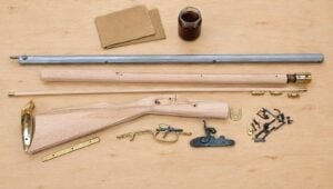 Traditions Kentucky rifle kit parts laid out flat: barrel, unfinished stock pieces, lock and brass furniture