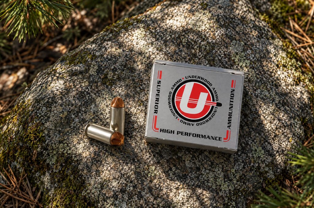 Underwood Xtreme Defender 10mm Auto 115 grain box and cartridges on a granite boulder in a pine forest