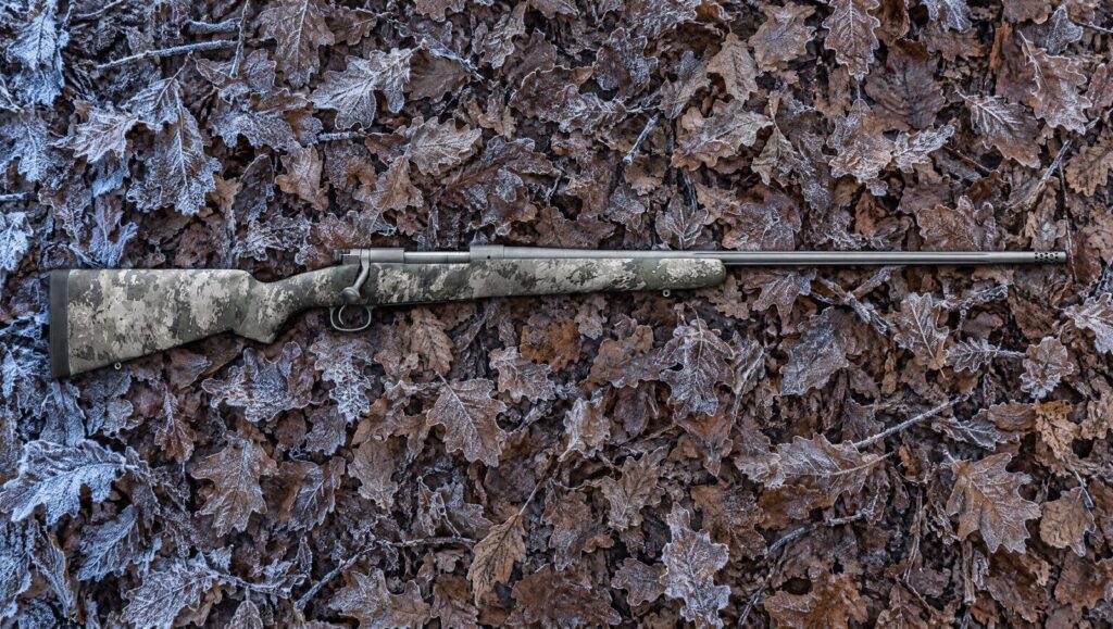 Winchester Model 70 Extreme TrueTimber VSX MB with VSX camo stock and Tungsten Cerakote barrel lying flat on frosted oak leaves