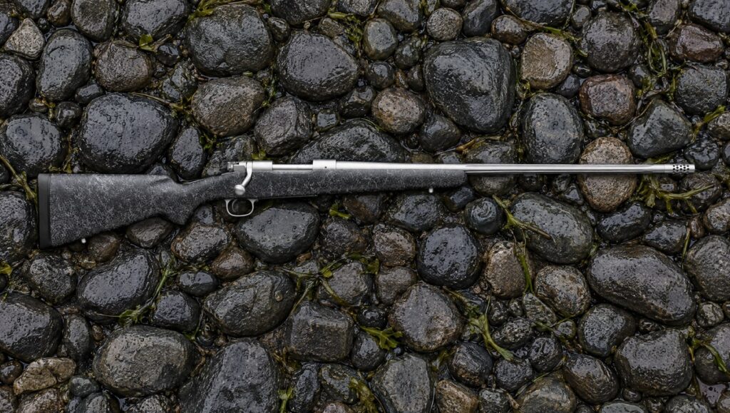 Winchester Model 70 Extreme Weather MB with stainless fluted barrel, muzzle brake and gray composite stock lying flat on wet river stones