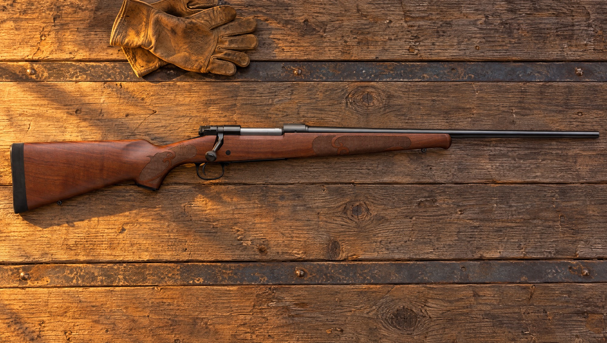 Winchester Model 70 Featherweight lying flat on the weathered wood planks of a truck tailgate in low evening sun, right side, with walnut stock and blued barrel