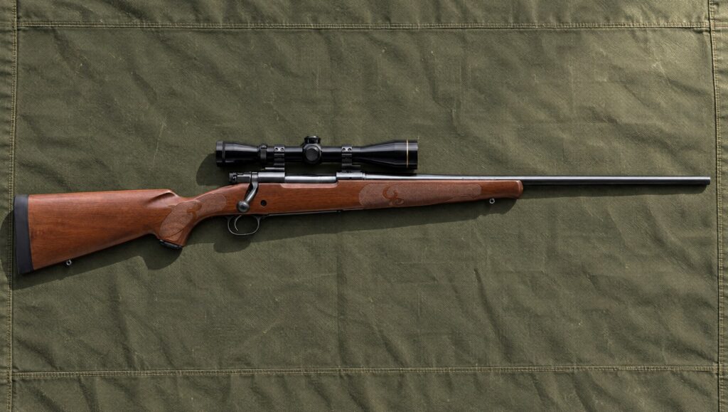 Winchester Model 70 Featherweight with a scope mounted, lying flat on a green canvas shooting mat, right side showing the bolt handle and Schnabel fore-end