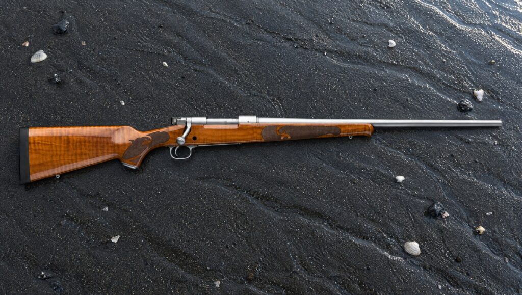 Winchester Model 70 Featherweight Stainless Dark Maple with gloss maple stock and stainless barrel lying flat on wet black sand
