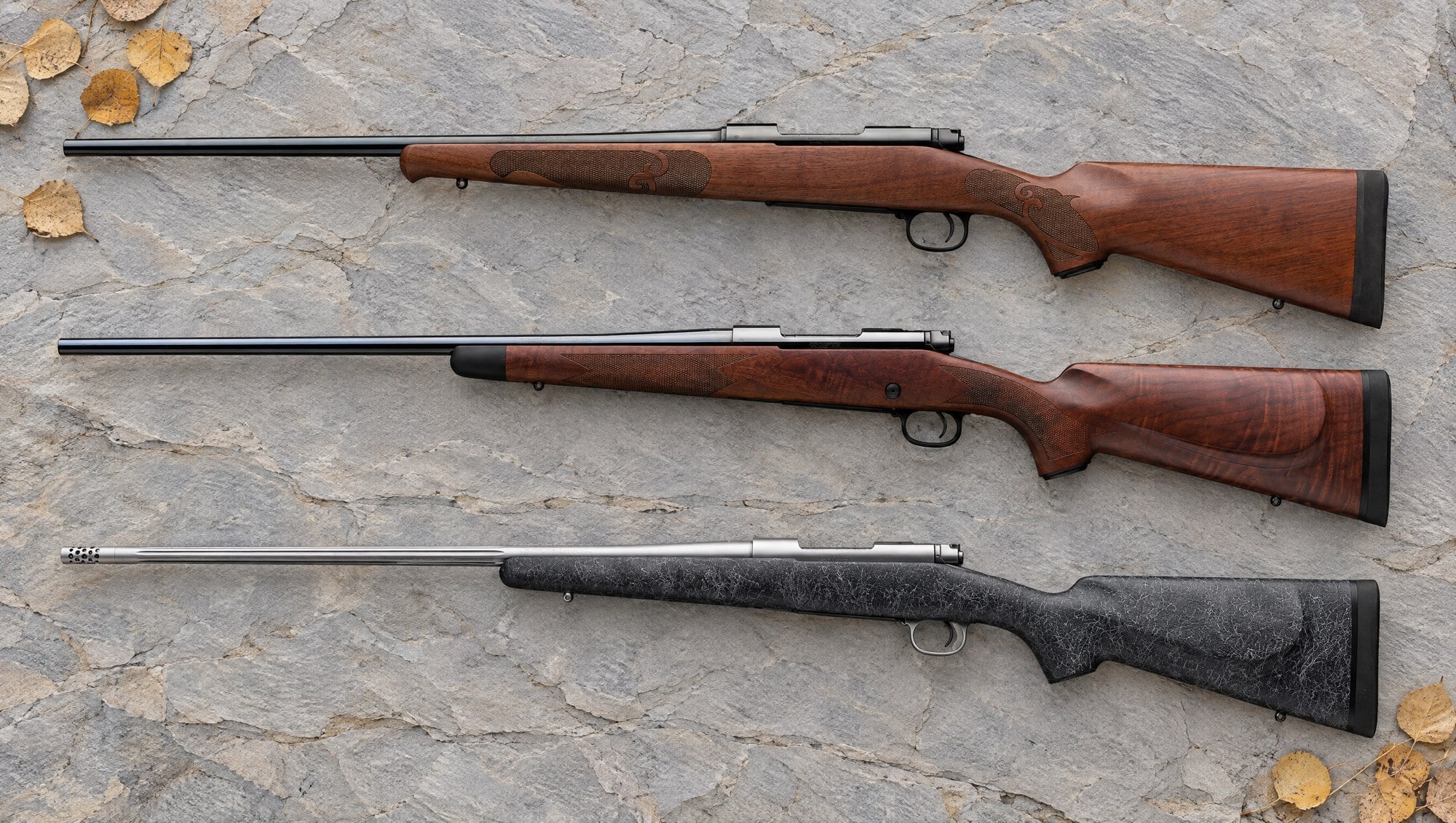 Winchester Model 70 models compared: a walnut Featherweight, a Super Grade and a stainless Extreme Weather MB lying flat on gray slate